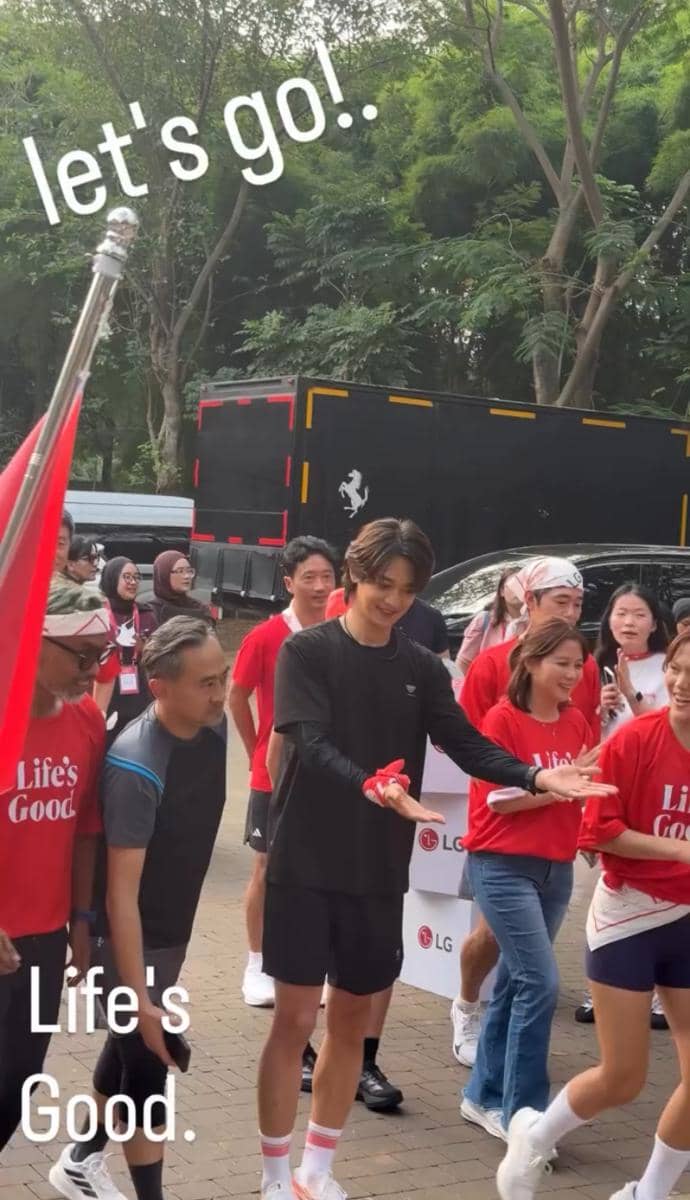 Seorang pria mengenakan pakaian olahraga hitam berlari bersama peserta lain yang memakai kaus merah bertuliskan Life's Good di area luar ruangan.