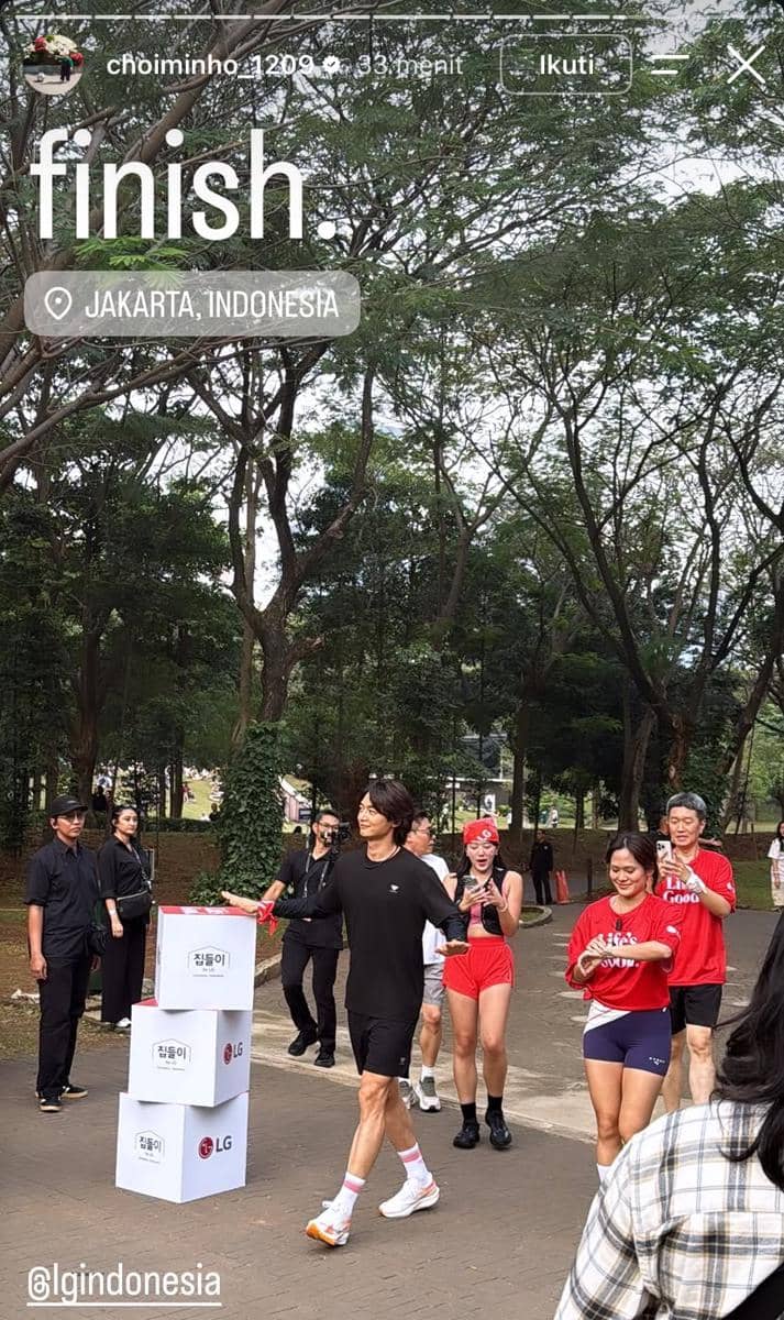 Seorang pria mengenakan pakaian olahraga hitam melintasi garis finis di area luar ruangan GBK Jakarta bersama peserta lain.