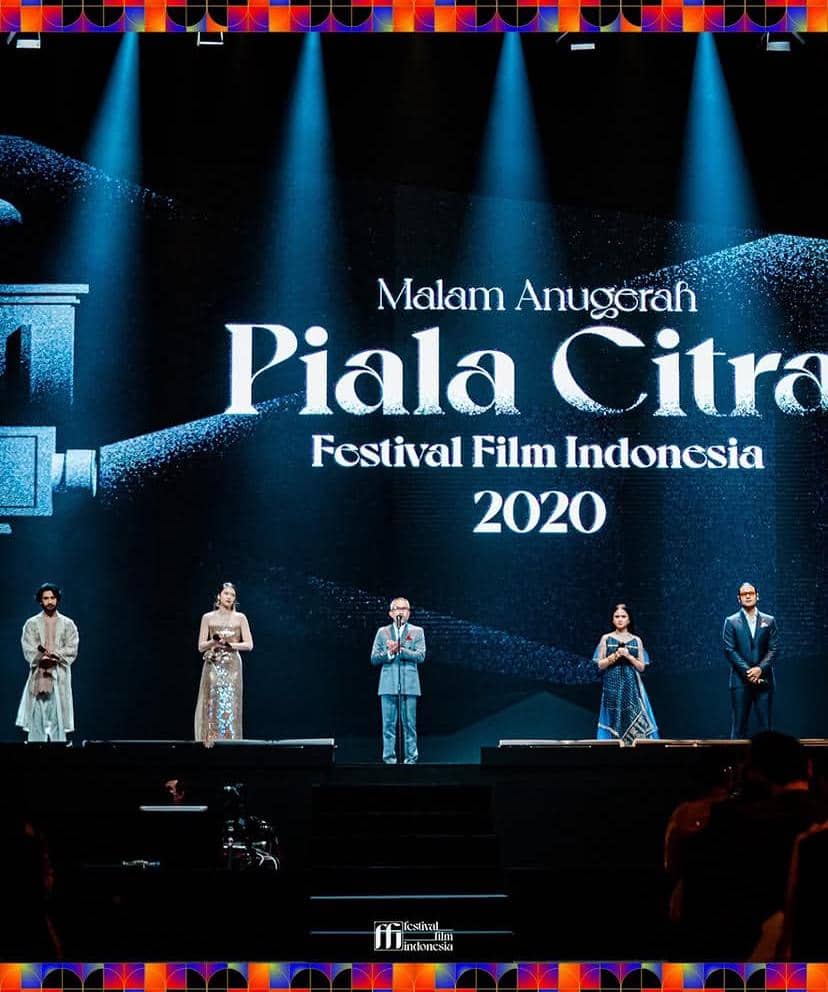 Lima orang berdiri di atas panggung dengan latar tulisan Malam Anugerah Piala Citra Festival Film Indonesia 2020 yang diterangi sorotan lampu biru.
