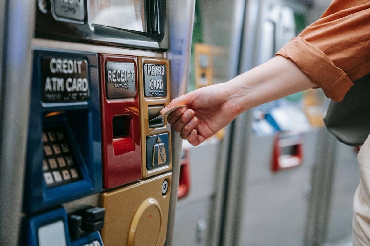 Seseorang memasukkan kartu ke mesin tiket otomatis berwarna-warni untuk melakukan transaksi di tempat umum.