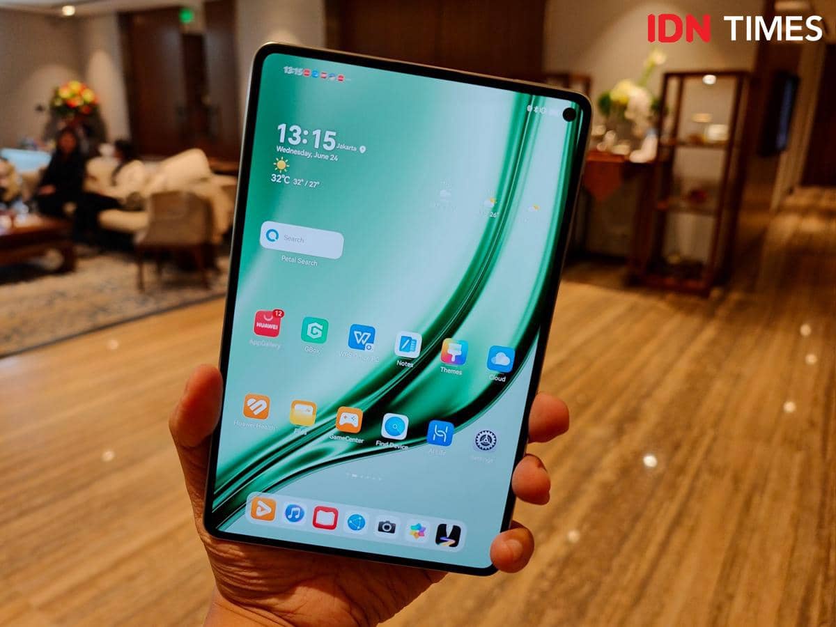 Seseorang memegang tablet HUAWEI MatePad Mini dengan layar menyala menampilkan antarmuka aplikasi di ruangan dengan pencahayaan hangat.