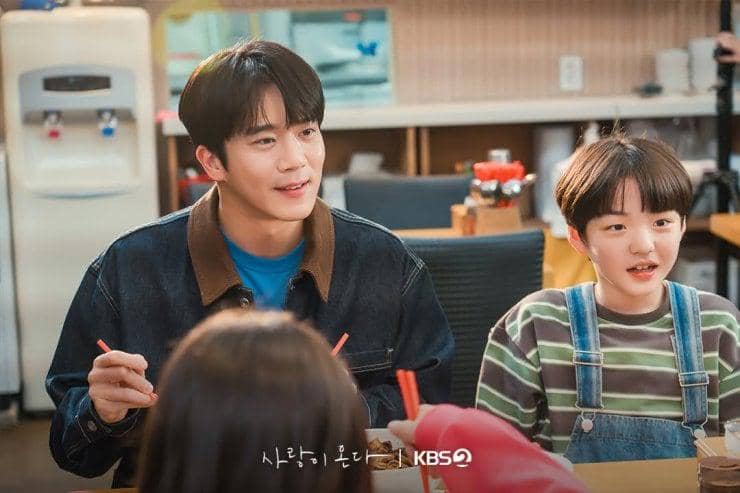 Adegan dua karakter sedang duduk di meja makan sambil berbincang dan tersenyum dalam drama Love on the Menu.