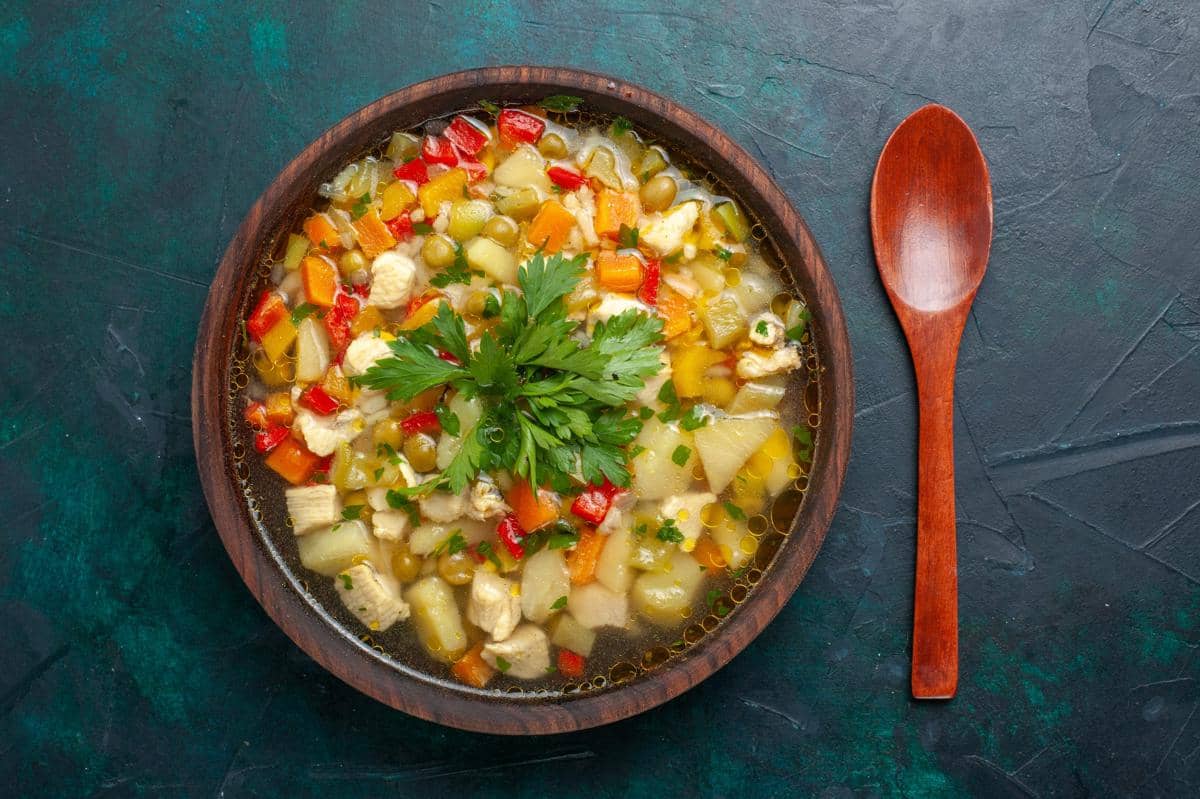 Semangkuk ribollita berisi sayuran berwarna-warni seperti wortel, kentang, paprika, dan kacang polong dengan hiasan daun peterseli segar.