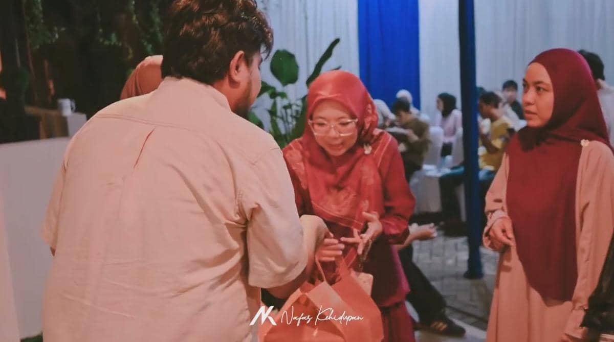 Beberapa orang berbincang dan saling memberikan bingkisan dalam acara akikah dengan suasana hangat dan dekorasi sederhana.
