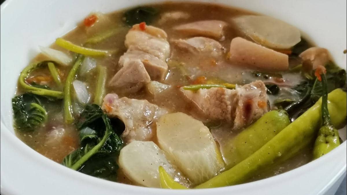 Semangkuk sinigang na baboy berisi potongan daging babi, sayuran hijau, lobak, cabai hijau, dan kuah asam gurih.