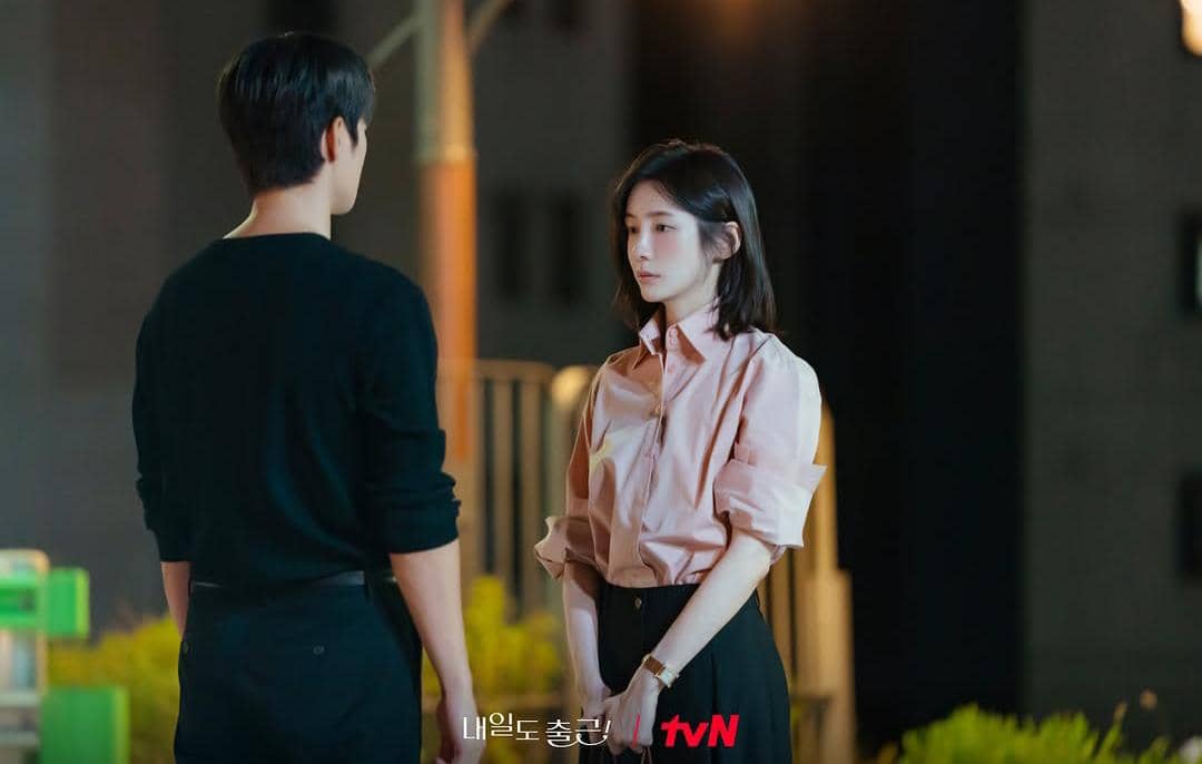 Dua orang berdiri saling berhadapan di malam hari dengan ekspresi serius dalam cuplikan drama See You at Work Tomorrow.
