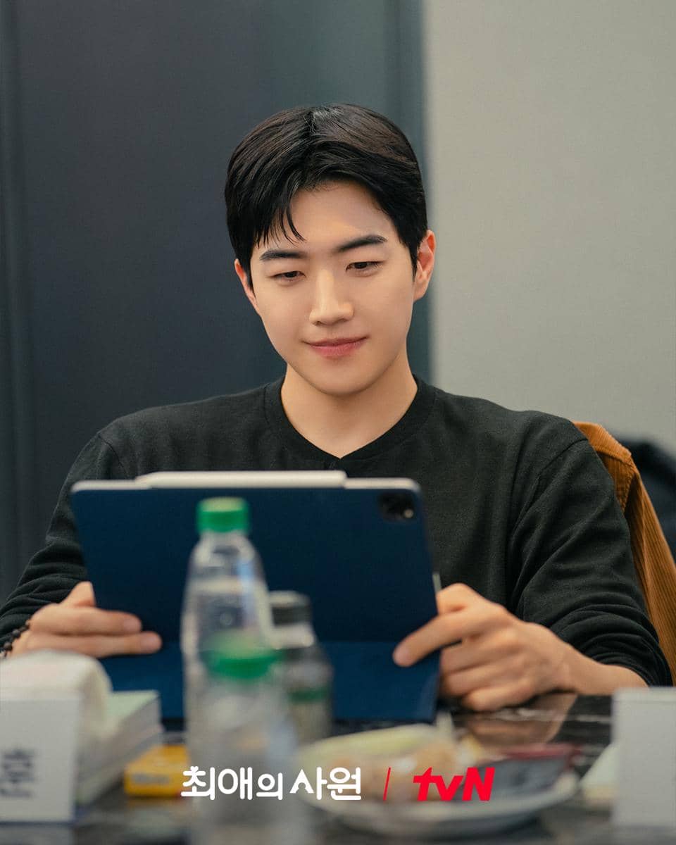 Seorang pria mengenakan kaus hitam sedang membaca naskah di tablet saat sesi pembacaan naskah drama My Bias, My Boss produksi tvN.