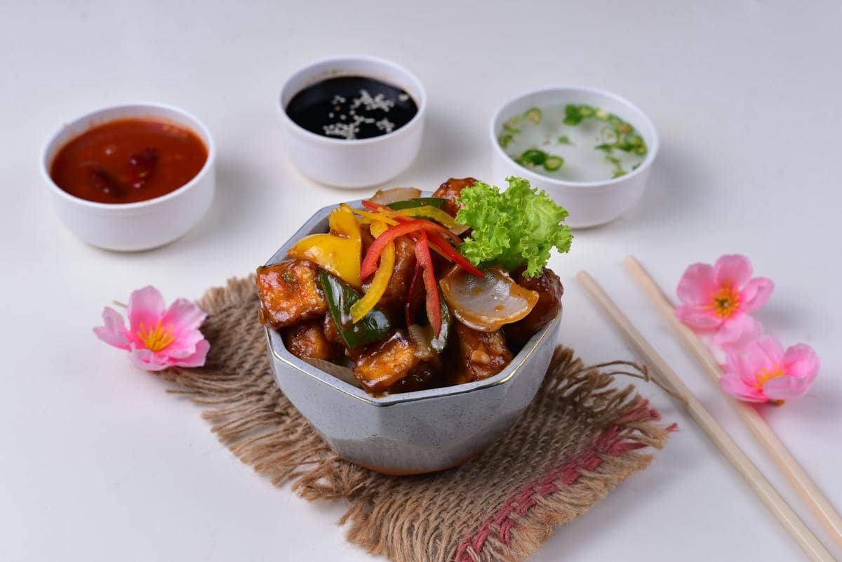 Semangkuk ayam sayur saus tiram dengan potongan paprika, bawang, dan hiasan selada disajikan bersama tiga mangkuk saus pendamping.
