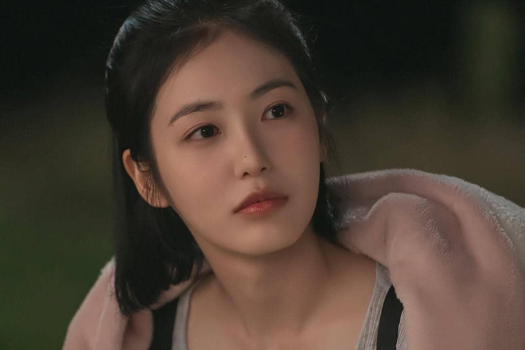 Seorang perempuan berambut hitam pendek mengenakan jaket berwarna lembut terlihat menatap ke samping dalam adegan drama Doctor on the Edge.