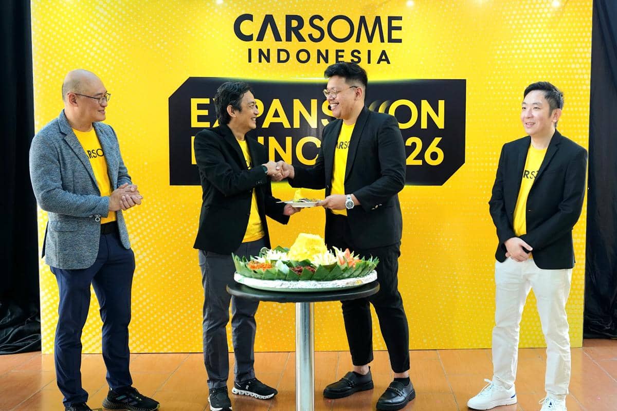 Beberapa pria berpakaian formal dengan kaus kuning Carsome berjabat tangan di depan meja tumpeng dalam acara peluncuran Carsome Indonesia.