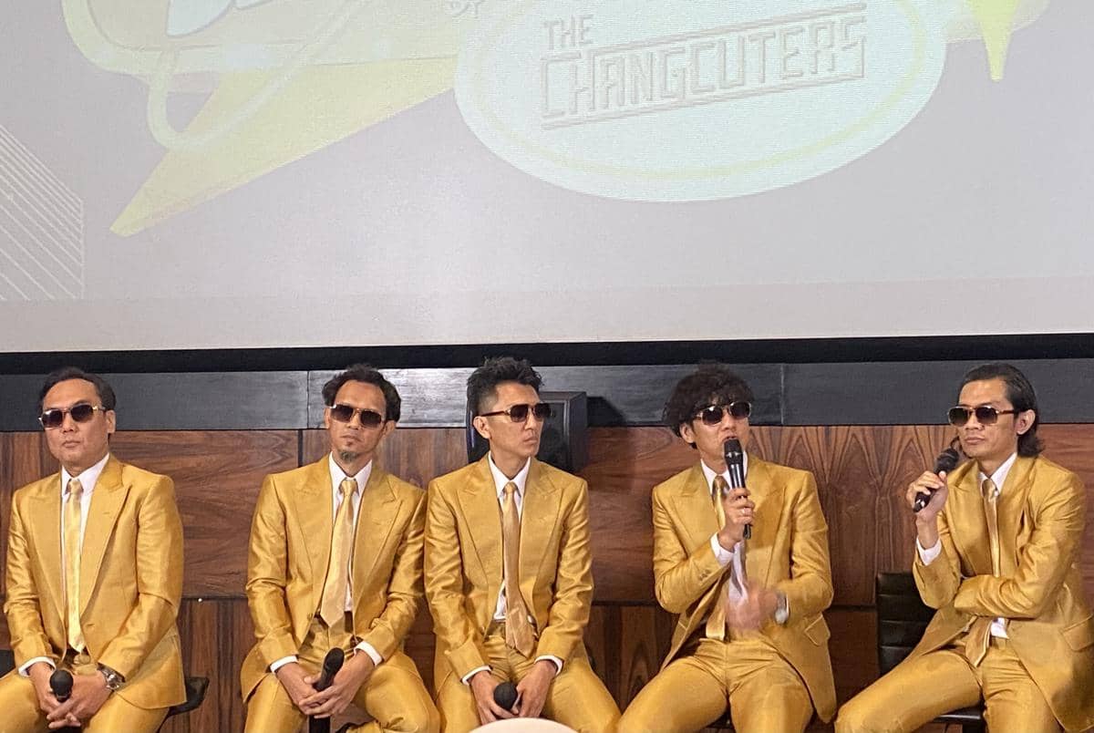 Lima pria mengenakan setelan jas emas dan kacamata hitam duduk berjejer di depan layar bertuliskan The Changcuters di Queens Head, Kemang.