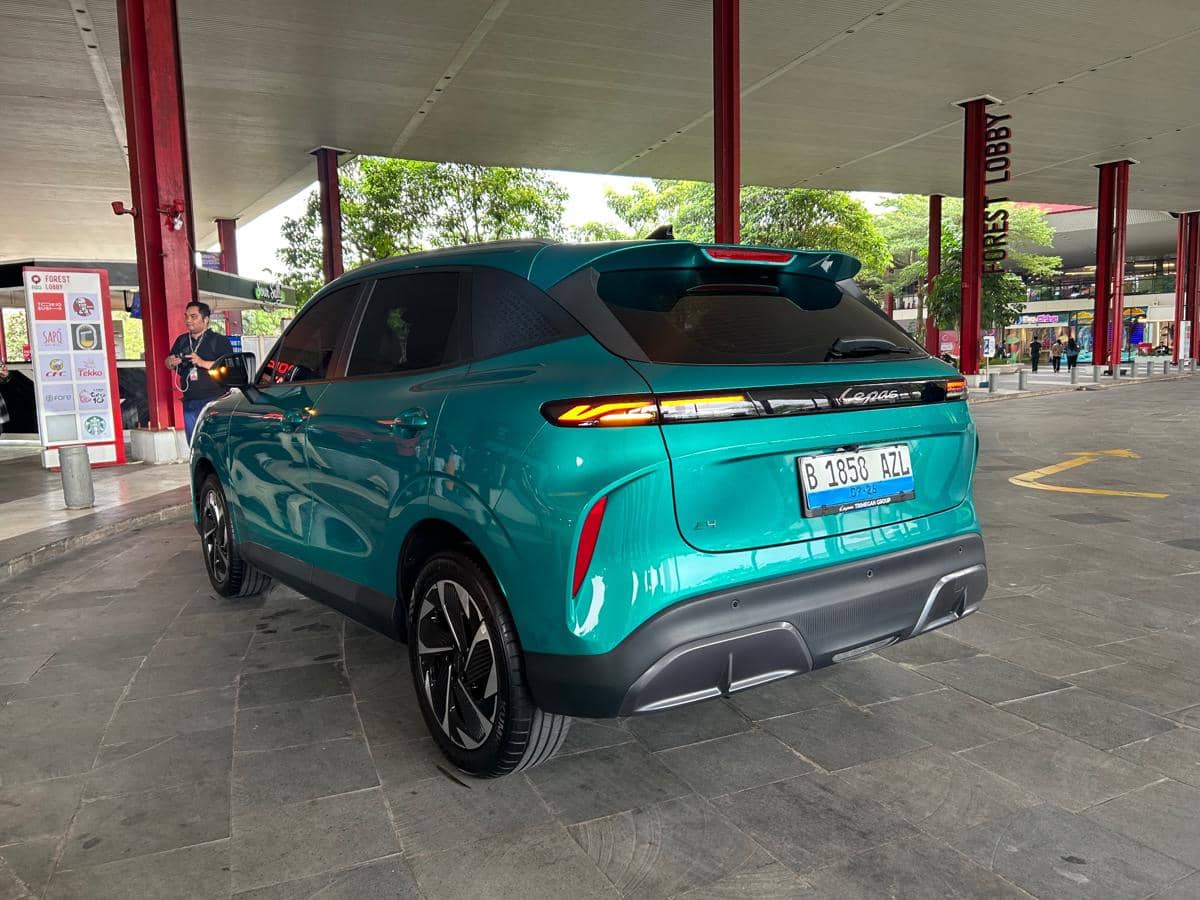Tampak belakang mobil listrik Lepas E4 EV berwarna hijau toska sedang terparkir di area lobi dengan latar tiang merah dan pepohonan.