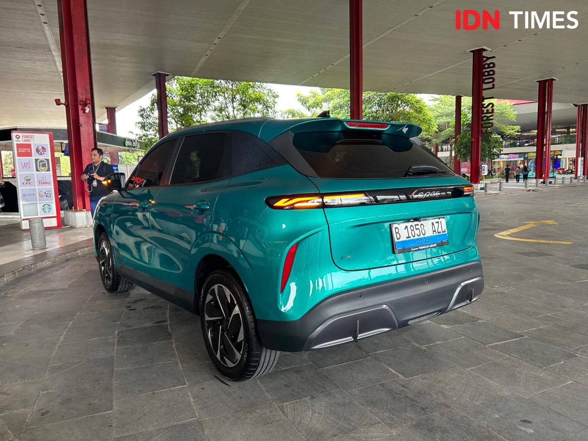 Tampak belakang mobil listrik Lepas E4 EV berwarna hijau toska sedang terparkir di area lobi dengan latar tiang merah dan pepohonan.