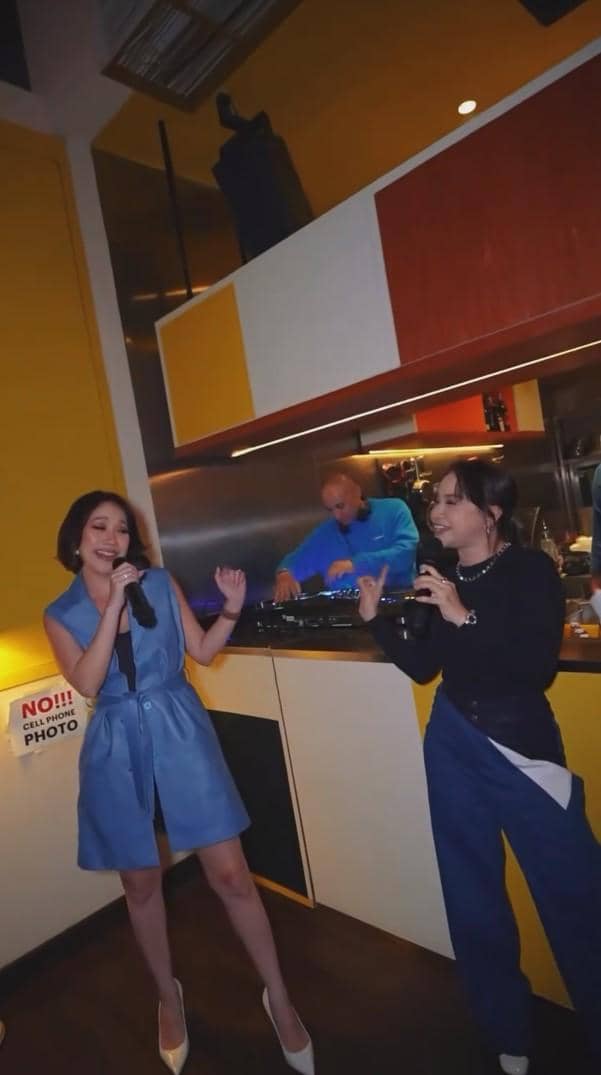 Dua wanita bernyanyi bersama dengan mikrofon di pesta perpisahan Indonesian Idol Season 14, diiringi DJ di latar belakang.