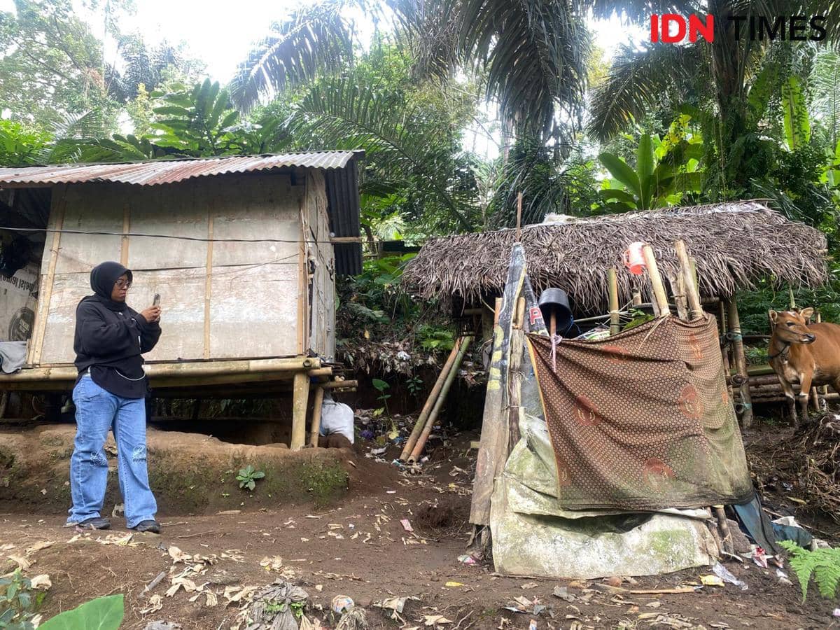 Seorang perempuan berdiri di depan rumah panggung sederhana dan tempat MCK beratap rumbia di Desa Mekarsari, Lombok Barat.