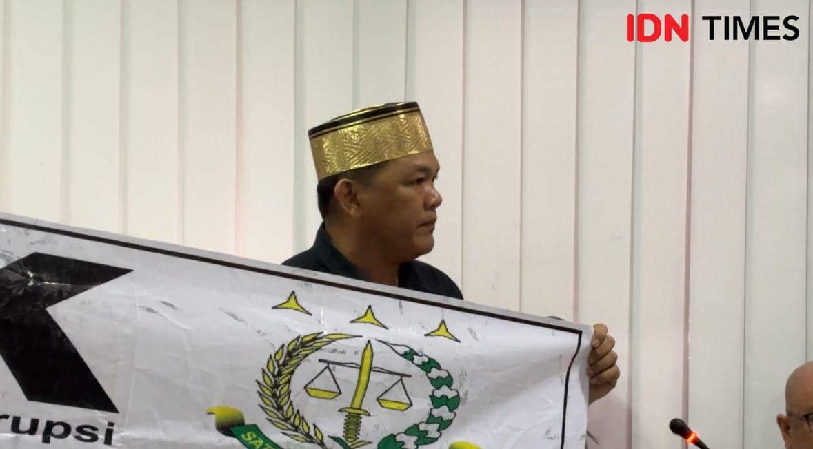 Seorang pria mengenakan songkok emas memegang spanduk bergambar lambang keadilan saat rapat dengar pendapat di DPRD Sulawesi Selatan.