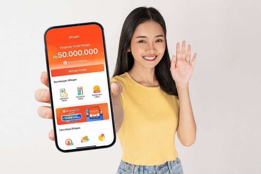 Seorang wanita mengenakan kaus kuning tersenyum sambil memperlihatkan layar ponsel yang menampilkan aplikasi SPinjam dari ShopeePay.