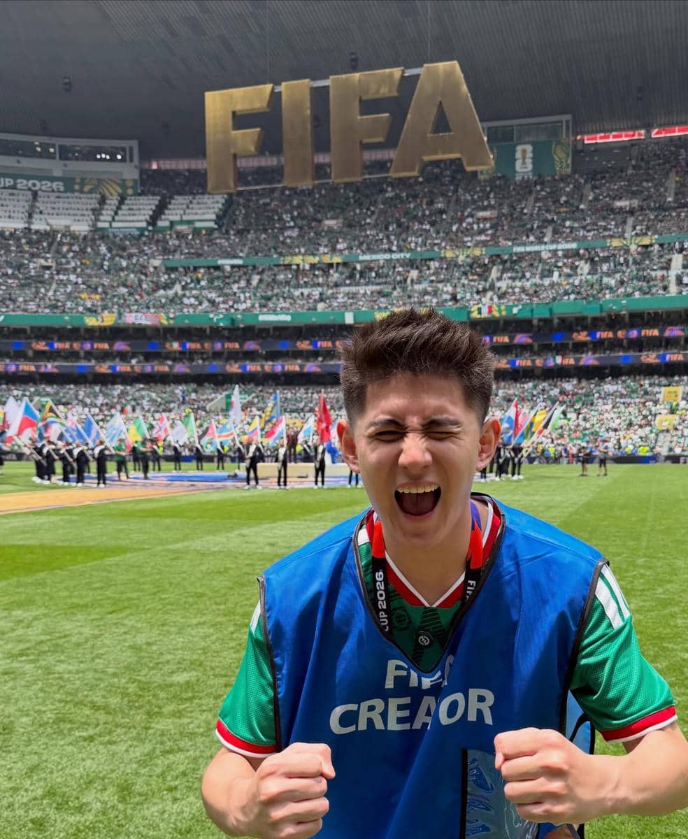 Seorang pria mengenakan rompi biru bertuliskan FIFA Creator berpose dengan ekspresi gembira di stadion penuh penonton saat Piala Dunia 2026.