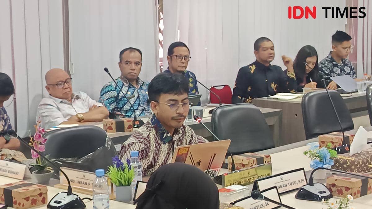 Seorang peserta rapat berbicara menggunakan mikrofon di ruang sidang DPRD Sulawesi Selatan, dihadiri beberapa orang dengan pakaian formal.