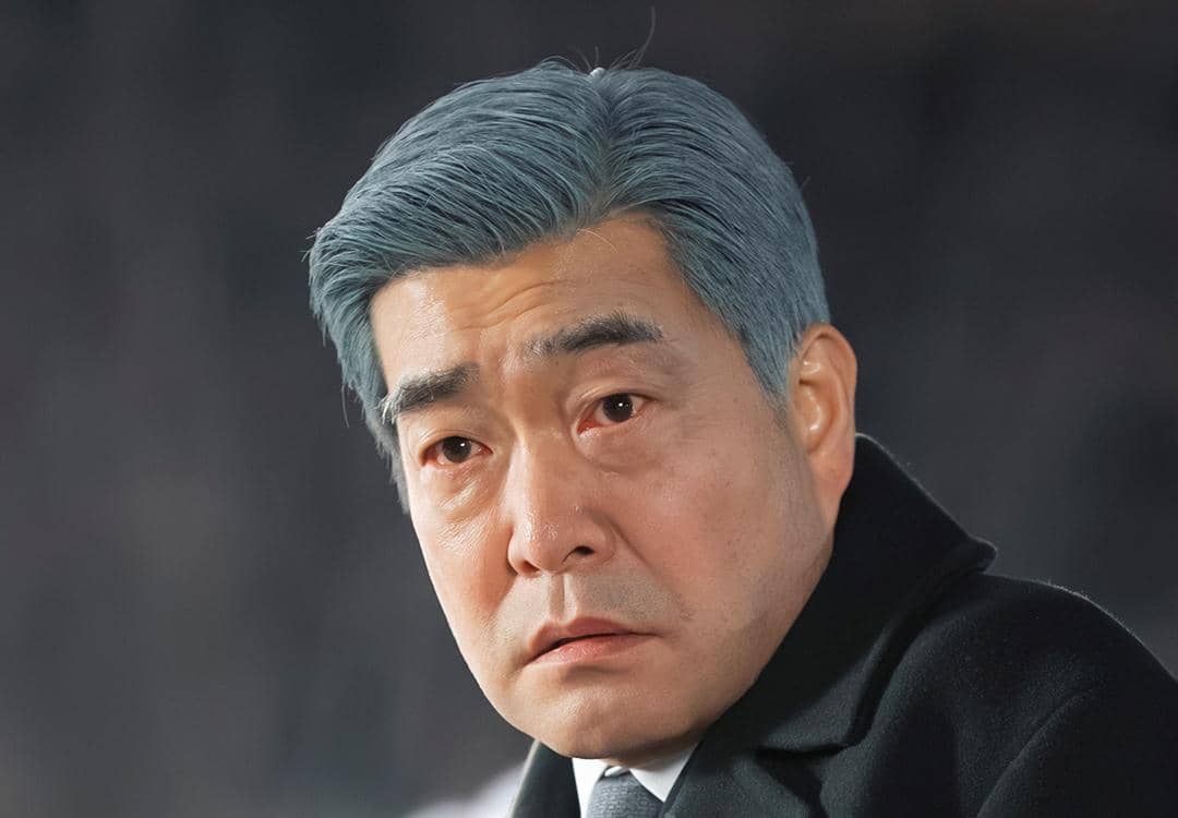 Seorang pria berambut abu-abu mengenakan jas hitam tampak serius dalam adegan drama Korea Reborn Rookie.