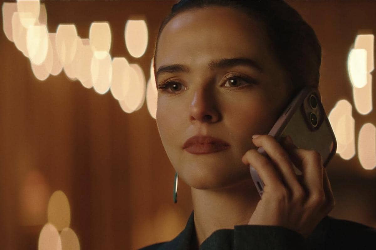 Seorang perempuan memegang ponsel di telinganya dengan ekspresi serius dalam adegan film Voicemails for Isabelle berlatar cahaya hangat.