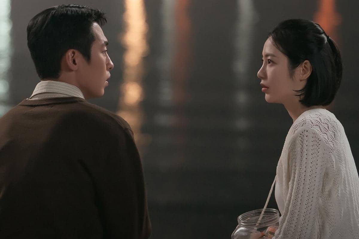 Dua orang duduk berhadapan di tepi air pada malam hari, berbincang dengan ekspresi serius dalam adegan drama Doctor on the Edge.
