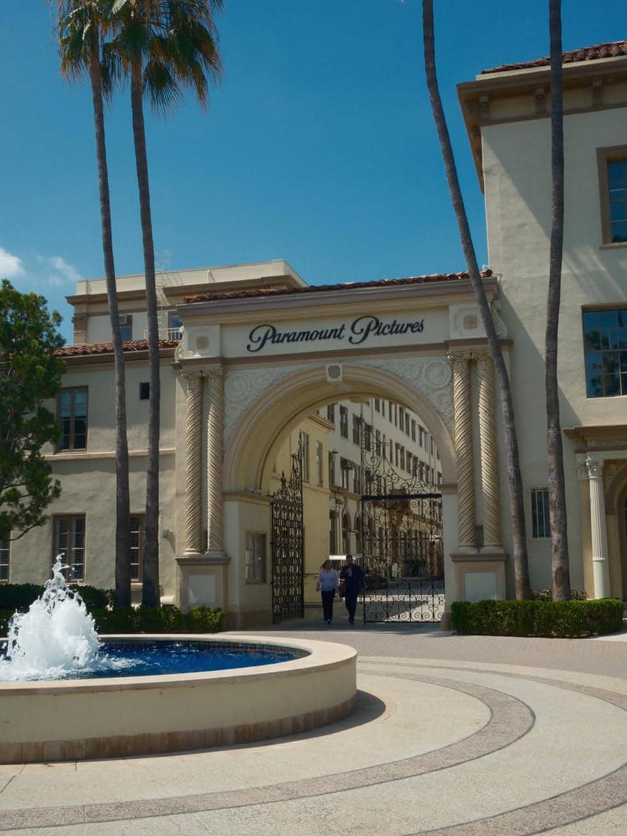 Gerbang ikonik Paramount Pictures di Hollywood dengan air mancur di depannya dan langit biru cerah di latar belakang.