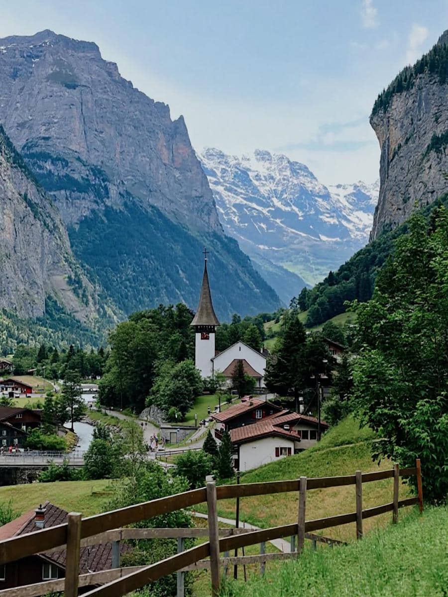 Pemandangan indah Desa Lauterbrunnen dengan gereja beratap runcing, rumah kayu, serta latar pegunungan bersalju di Swiss.