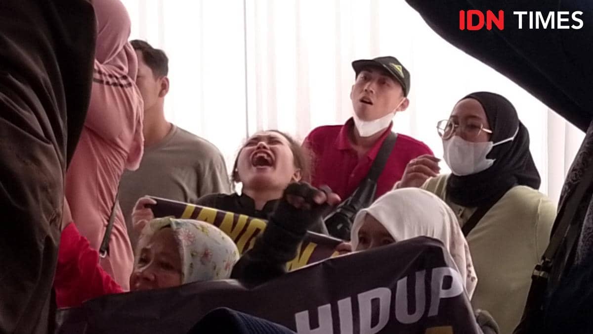 Seorang nasabah Mandiri Taspen Purwokerto berteriak histeris di tengah kerumunan orang yang tampak emosional dan memegang spanduk.