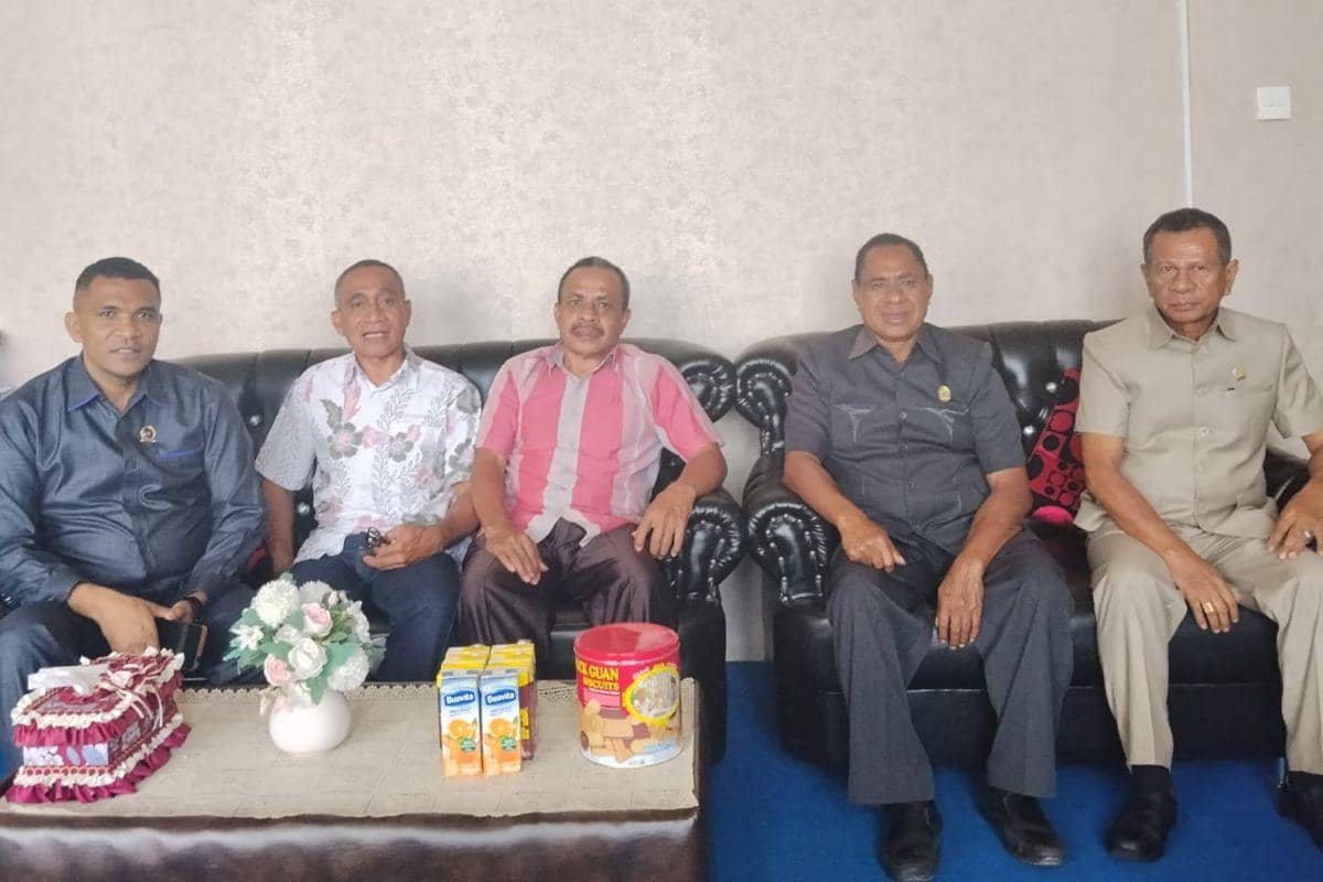 Lima pria duduk di sofa ruang tamu dengan meja berisi minuman kotak, toples biskuit, dan vas bunga di Kabupaten TTU.