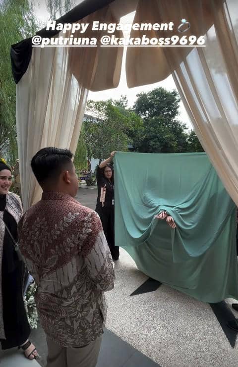Seorang pria mengenakan batik menghadiri acara lamaran di luar ruangan dengan dekorasi tirai dan kain hijau yang dipegang beberapa orang.