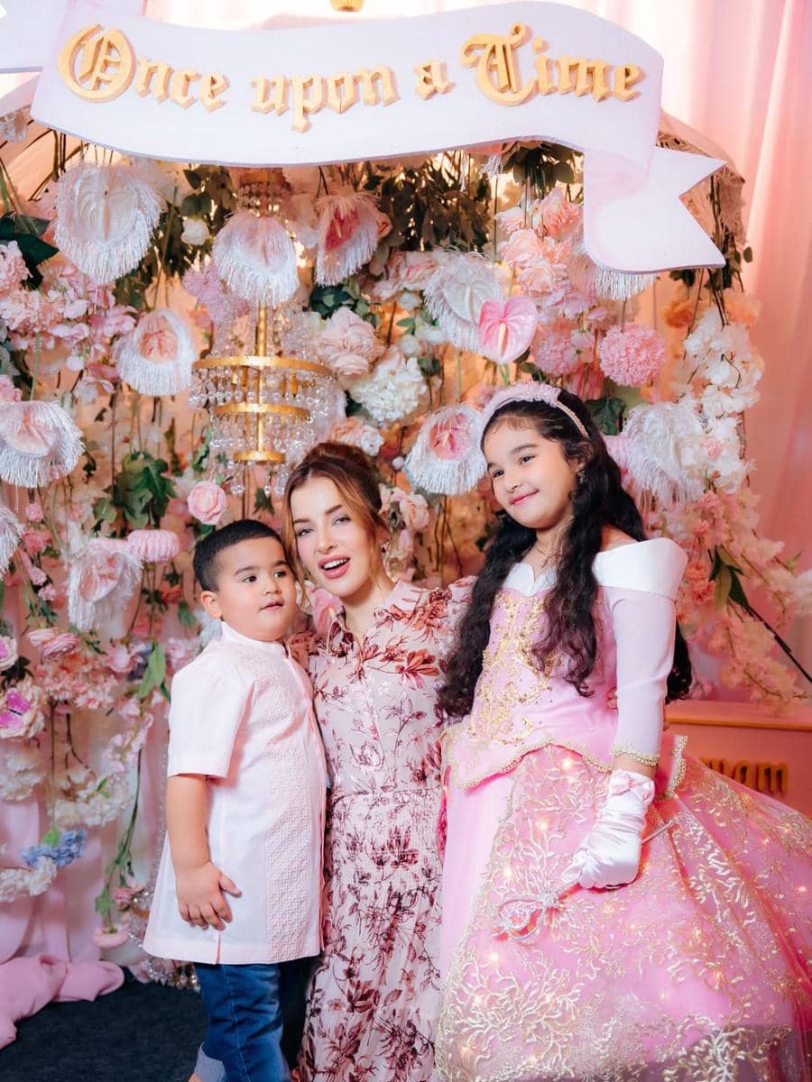Seorang wanita berpose bersama dua anak di pesta ulang tahun bertema dongeng dengan dekorasi bunga dan tulisan Once Upon a Time.