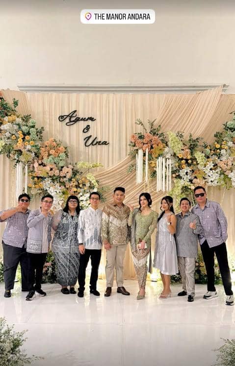 Pasangan mengenakan busana formal berpose bersama keluarga dan teman di acara lamaran dengan dekorasi bunga di The Manor Andara.