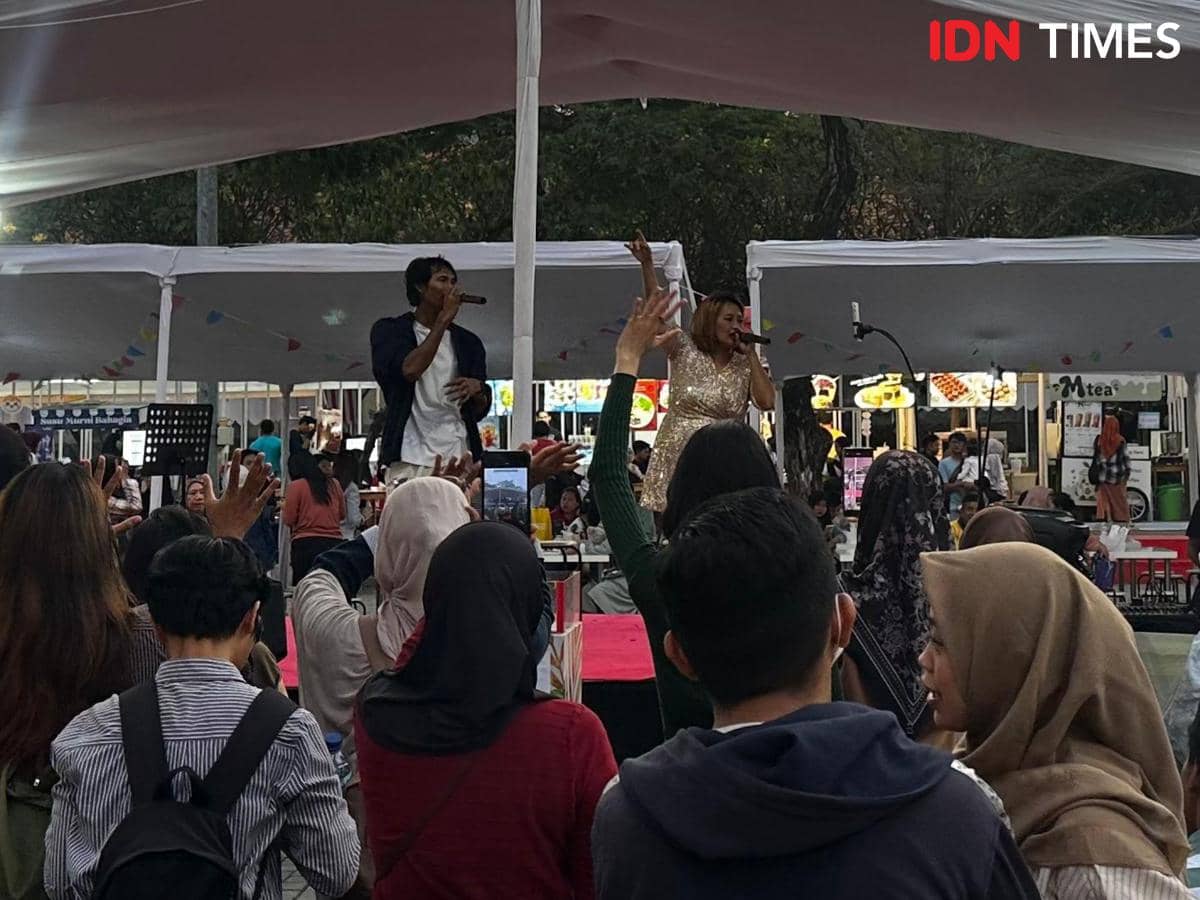 Seorang penyanyi tampil di atas panggung kecil di TangCity Mall bersama rekan duetnya, disaksikan penonton yang antusias mengangkat tangan.
