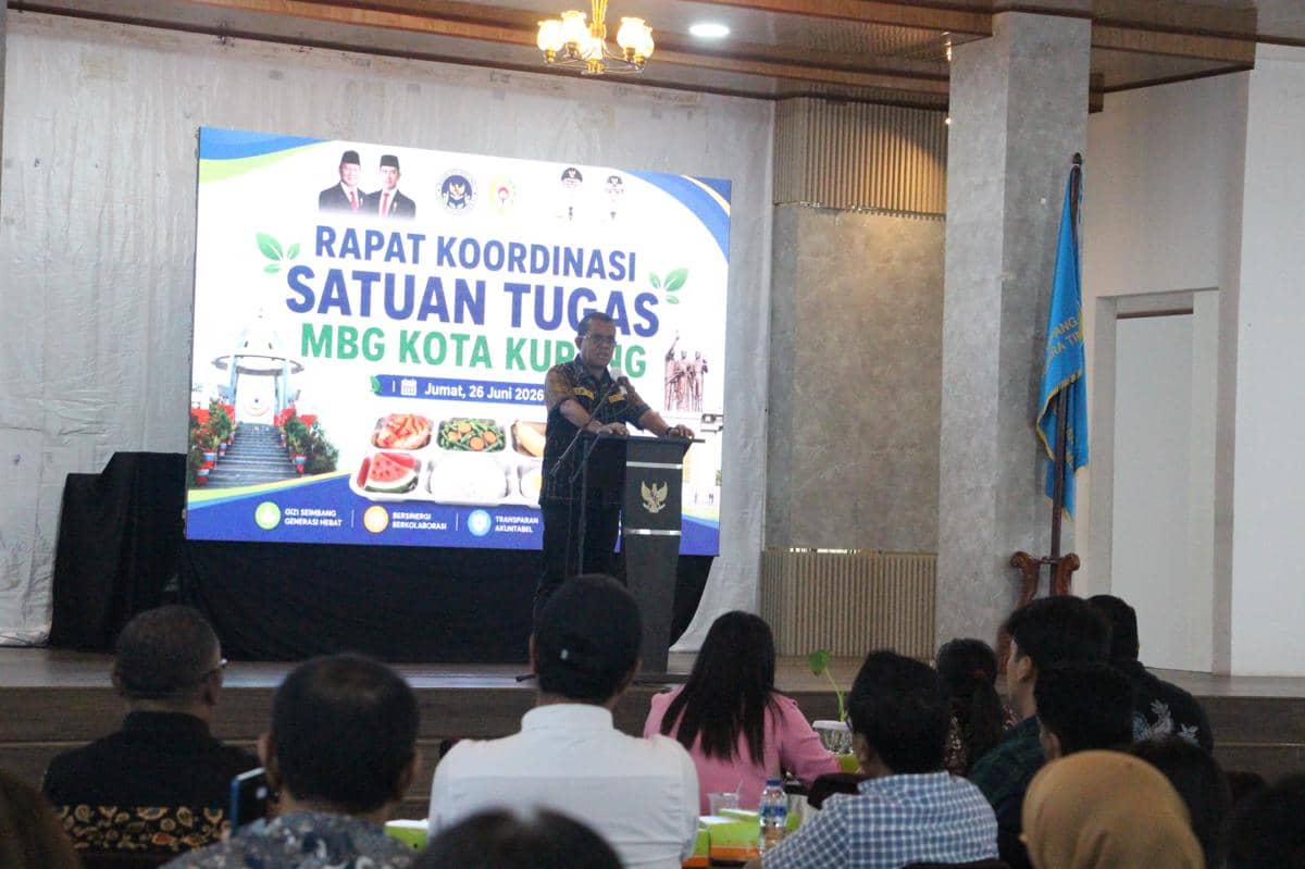 Gubernur NTT memberikan sambutan pada pembukaan rapat koordinasi Satuan Tugas MBG Kota Kupang di sebuah aula dengan peserta yang hadir.