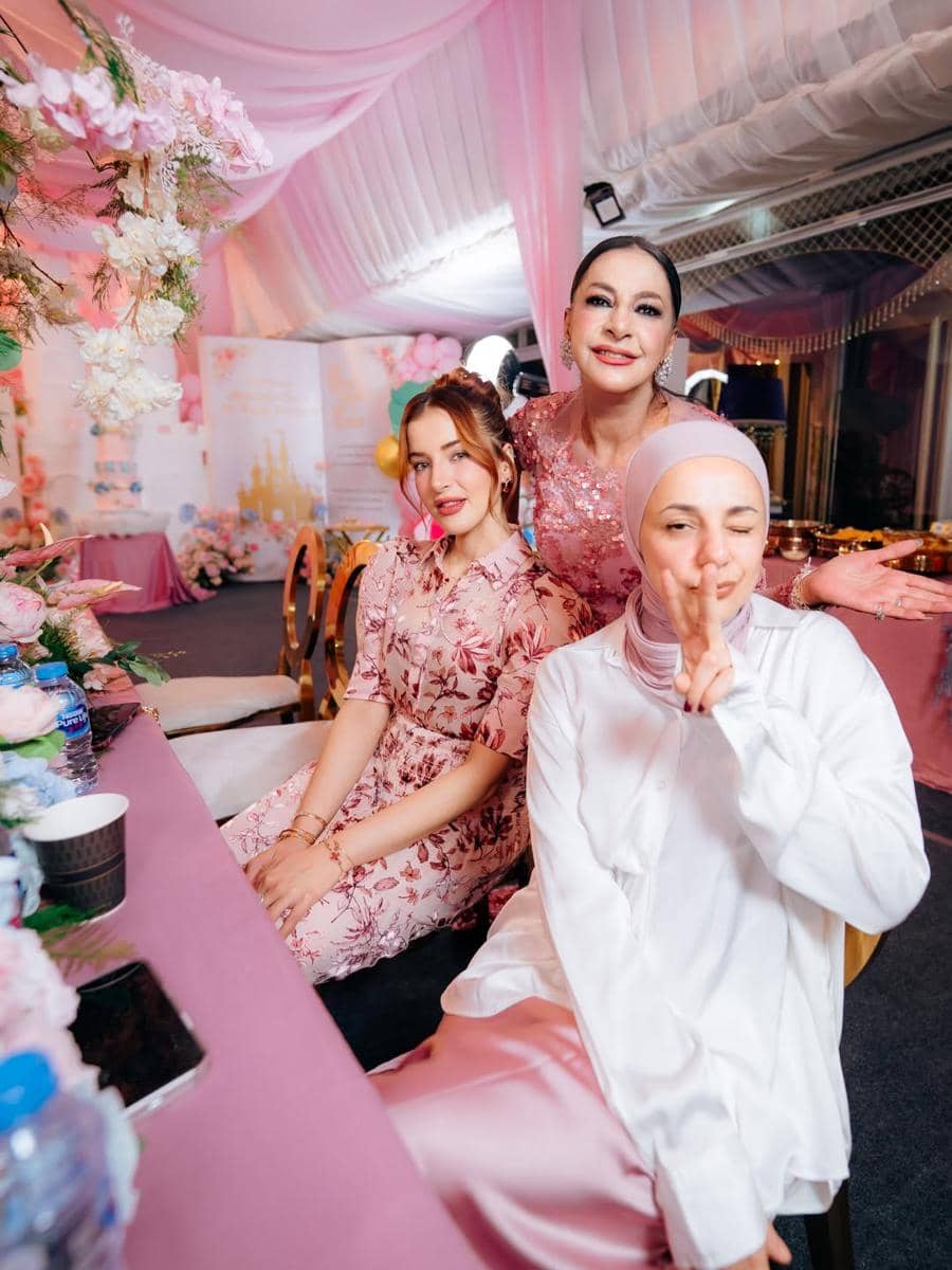 Tiga wanita berpose ceria di pesta ulang tahun bertema pink dengan dekorasi bunga dan kain tenda berwarna senada.