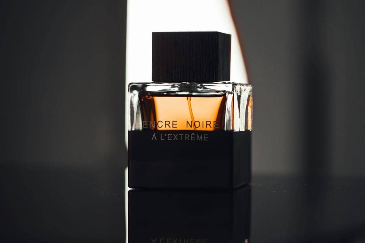 Botol parfum berwarna cokelat gelap dengan tutup hitam diletakkan di permukaan reflektif, menggambarkan perbedaan EDP dan EDT.