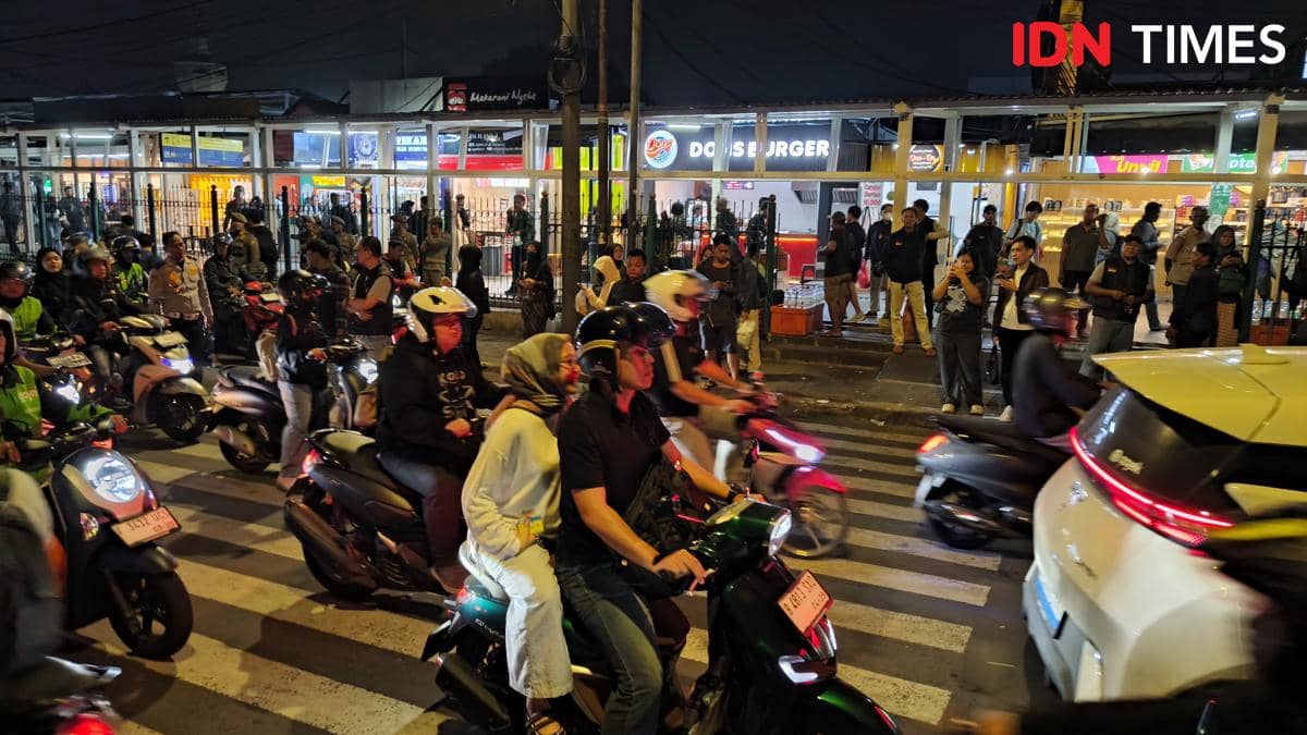 Keramaian pengendara motor dan pejalan kaki di area perlintasan dekat JPO Paledang, Bogor, pada malam hari dengan suasana padat.