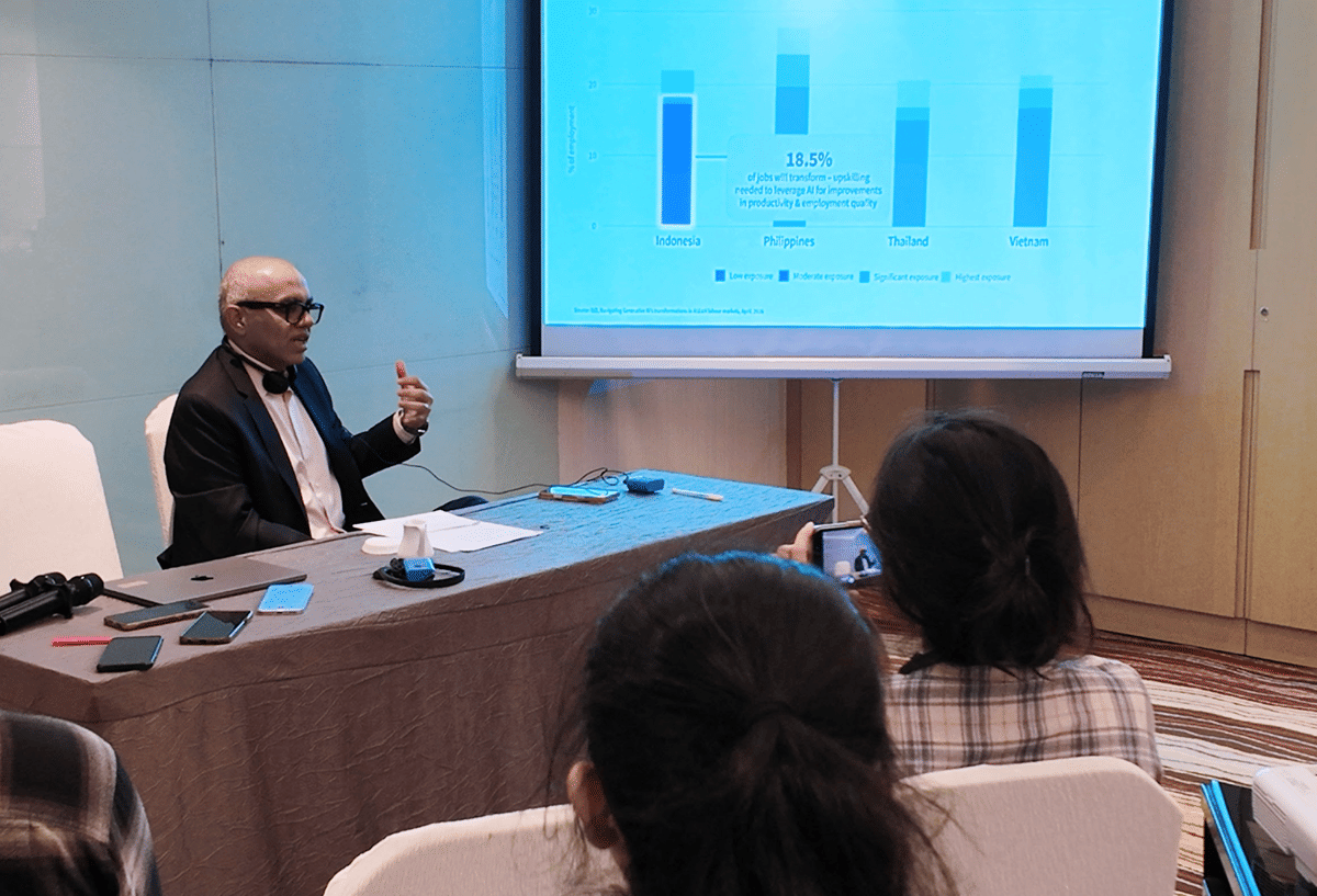 Seorang pembicara memberikan presentasi di depan peserta dengan layar proyektor menampilkan grafik perbandingan negara di Asia Tenggara.