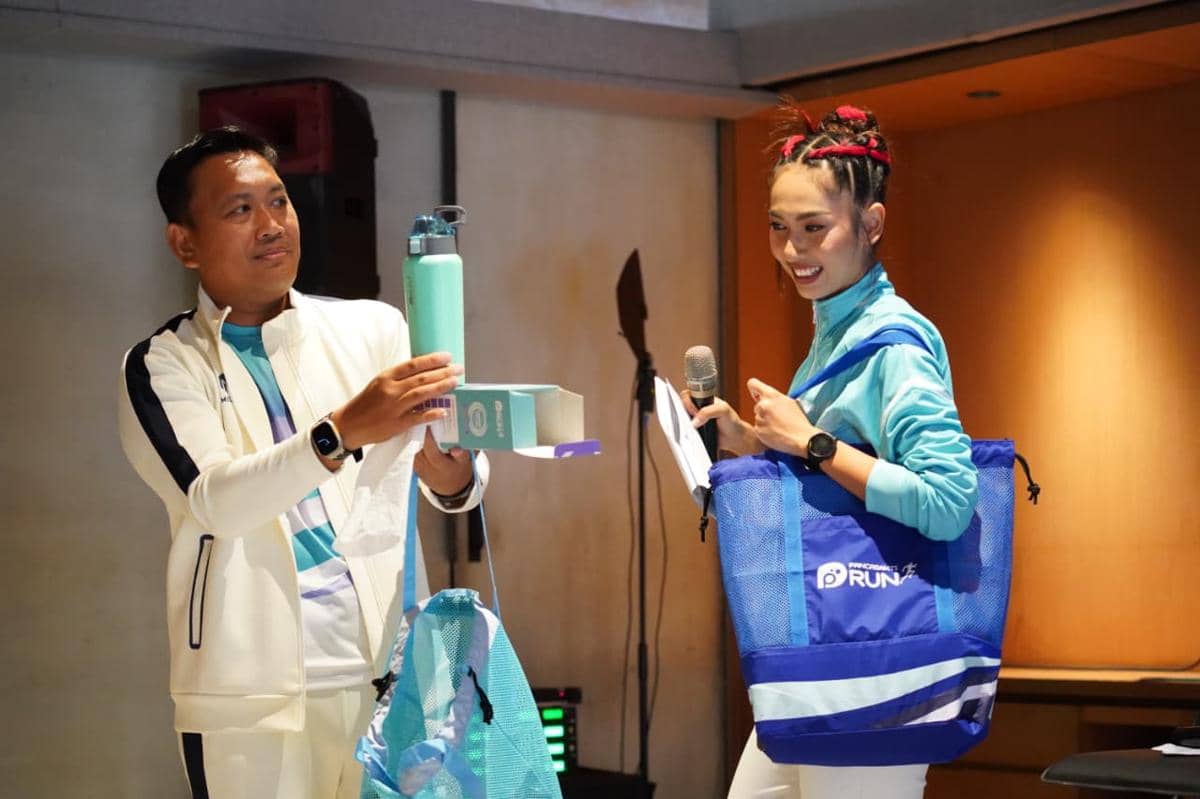 Dua orang mengenakan pakaian olahraga biru putih memperlihatkan botol minum dan tas bertuliskan Pancasakti Run 2026 di sebuah acara.