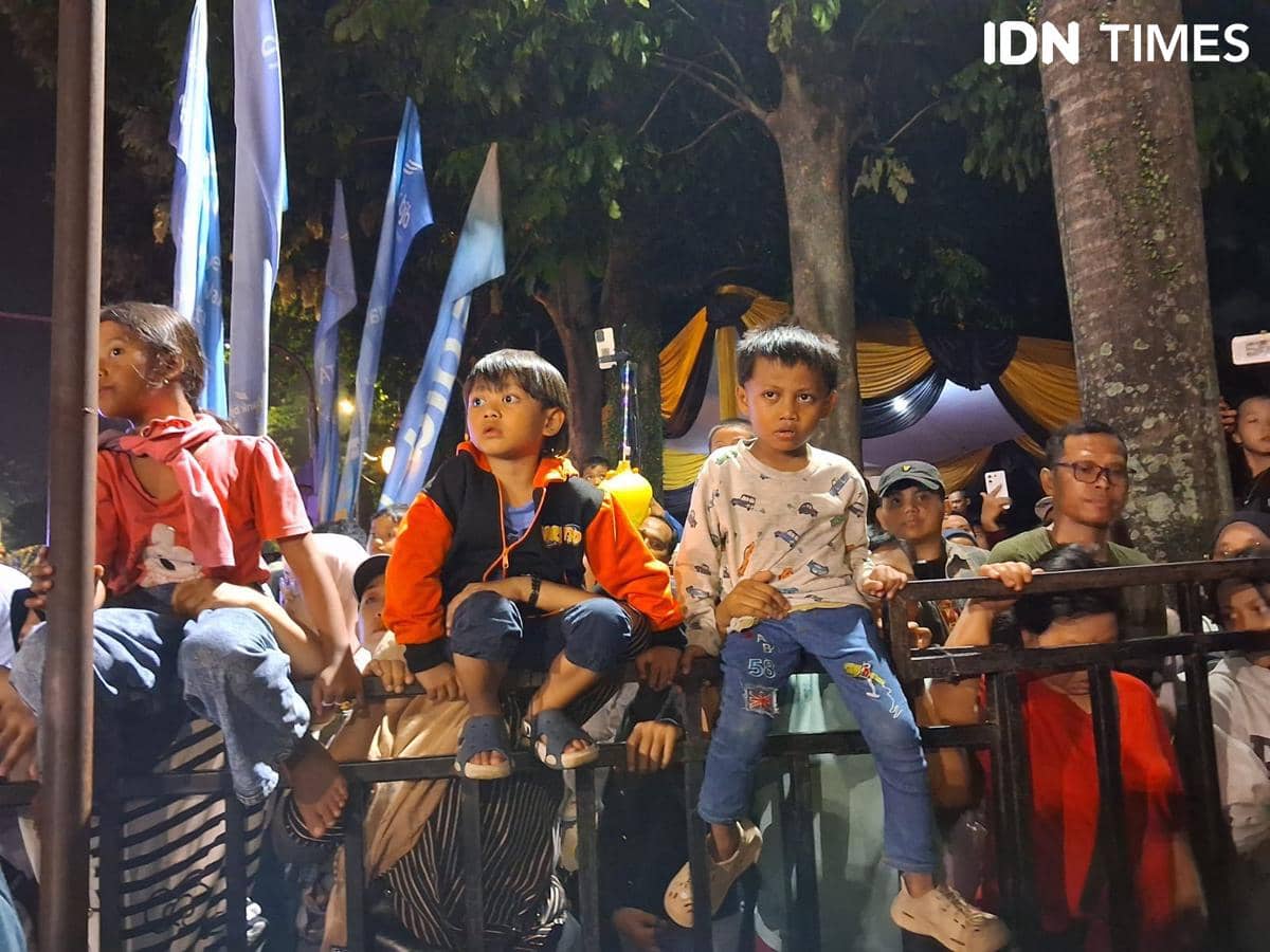 Anak-anak duduk di pagar bersama orang tua mereka menikmati kemeriahan perayaan Hari Jadi Bogor ke-544 pada malam hari.