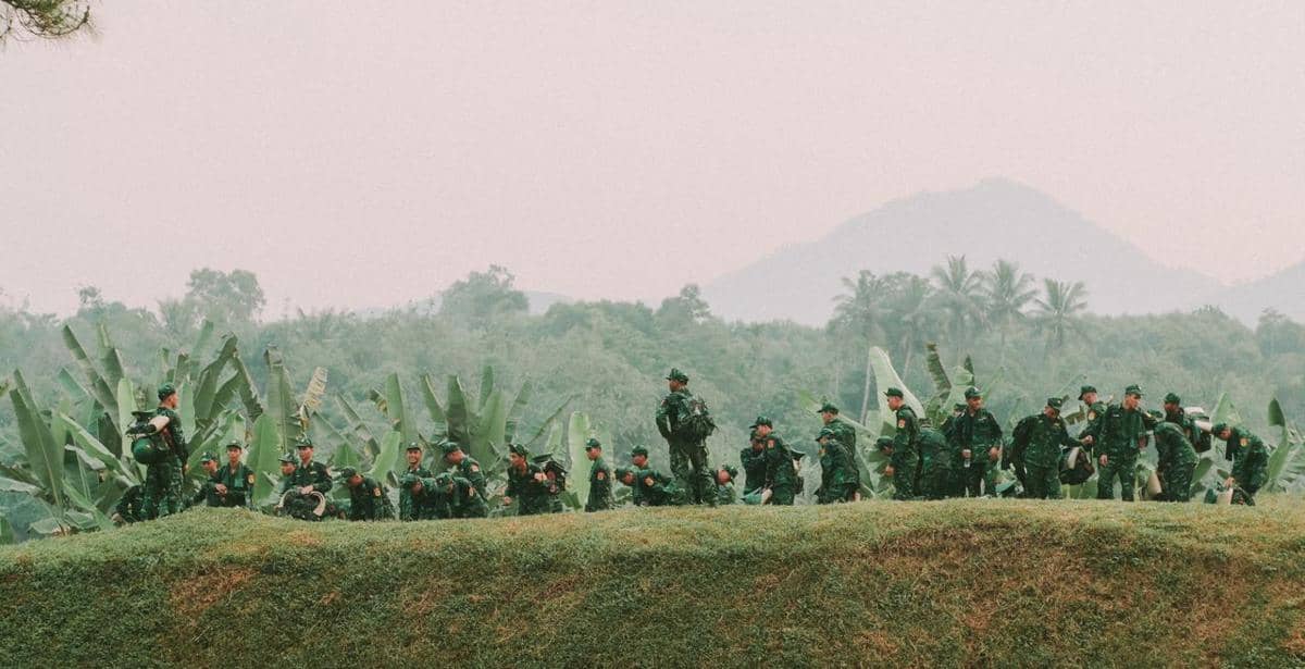 Sejumlah tentara berpakaian seragam hijau sedang melakukan latihan militer di area perbukitan dengan latar pepohonan dan gunung.