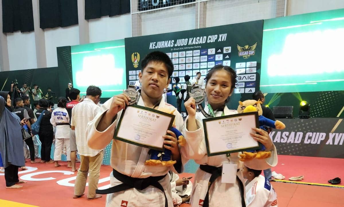 Dua atlet judo memegang sertifikat dan medali perak di arena Kejurnas Judo Kasad Cup XVI dengan latar belakang panggung dan peserta lain.