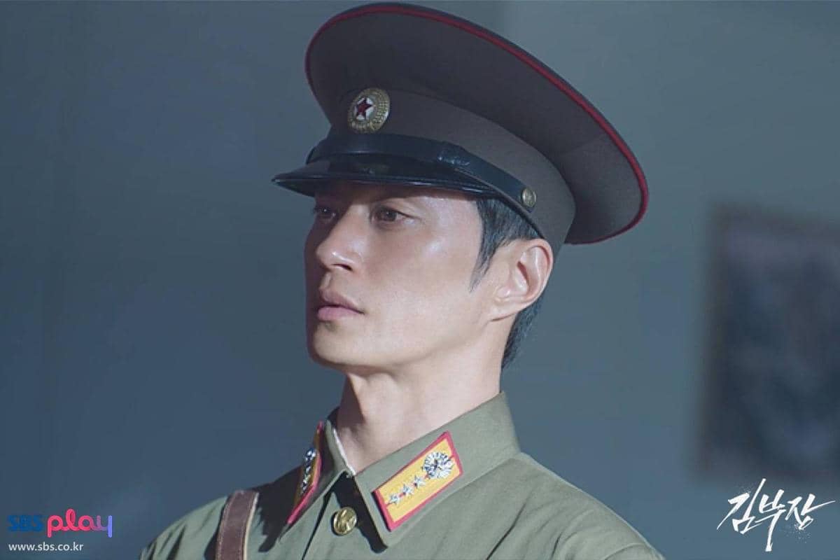 Seorang pria mengenakan seragam militer berwarna hijau dengan topi baret cokelat dalam cuplikan drama Korea Agent Kim Reactivated.