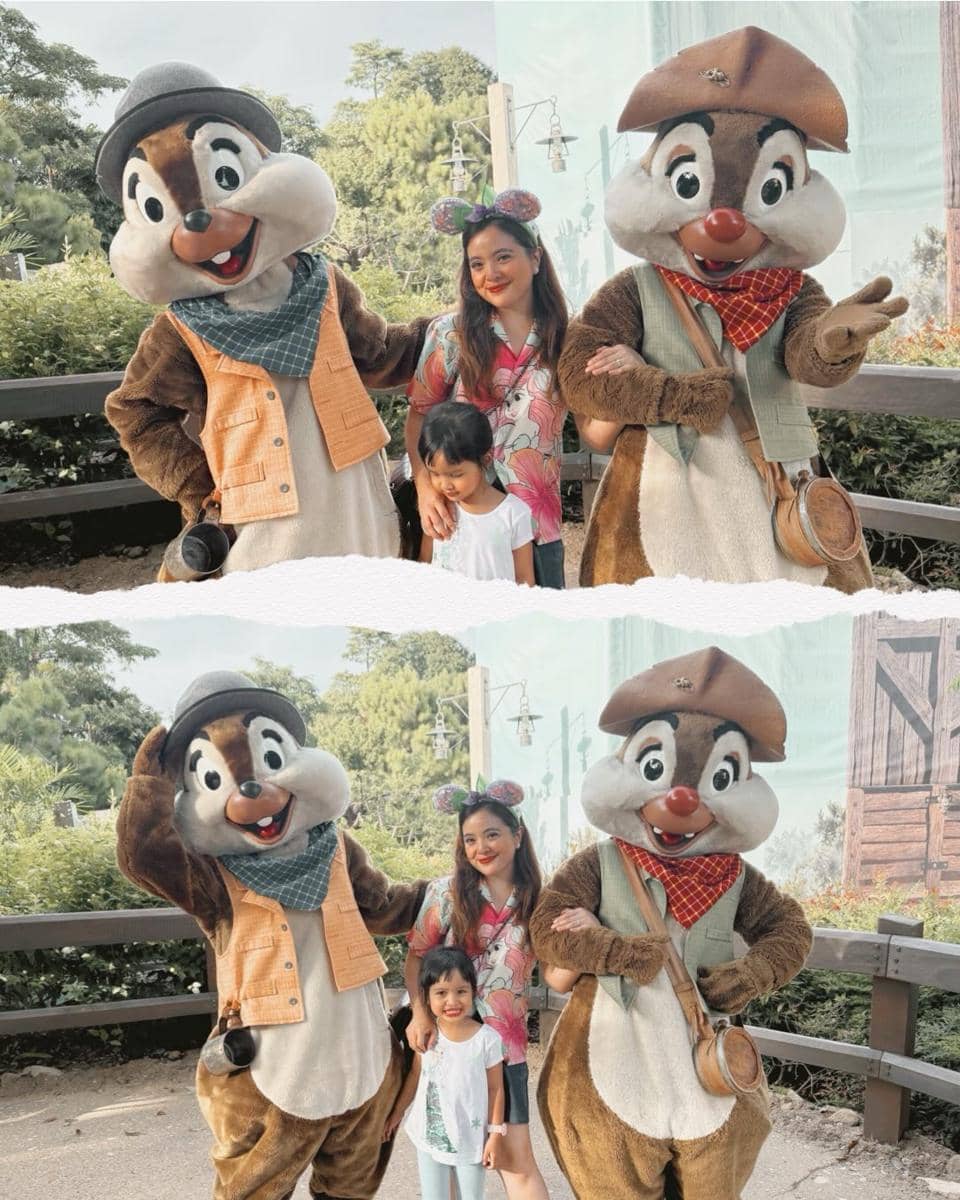 Seorang wanita dan anak kecil berpose bersama dua karakter Chip dan Dale di Disneyland Hong Kong dengan latar taman hijau.