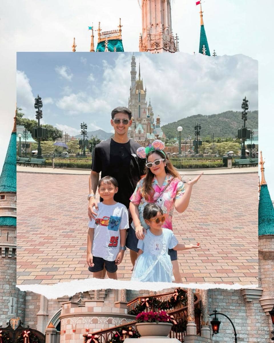 Sebuah keluarga berpose ceria di depan kastel ikonik Disneyland Hong Kong dengan latar langit cerah dan suasana liburan bahagia.