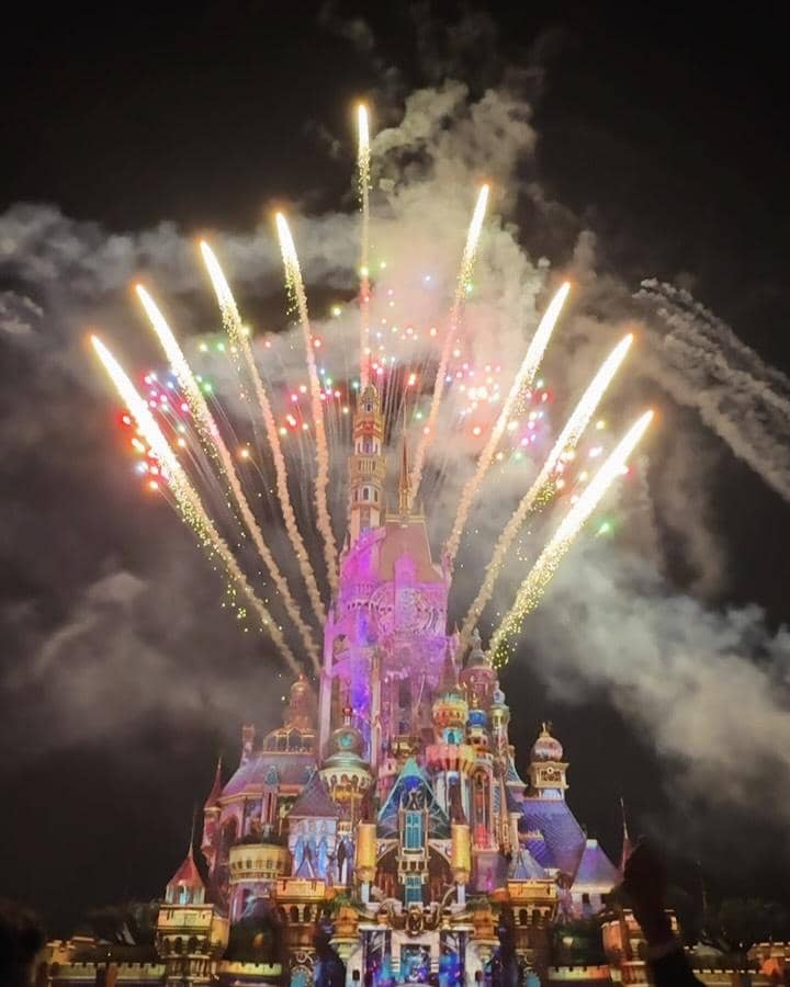 Pertunjukan kembang api berwarna-warni di atas kastel ikonik Disneyland Hong Kong pada malam hari dengan langit gelap dan cahaya gemerlap.