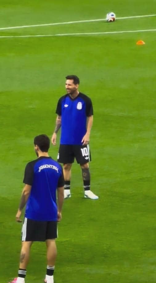 Seorang pemain sepak bola mengenakan jersey latihan biru dan hitam dengan nomor 10 di lapangan hijau bersama rekan setimnya.