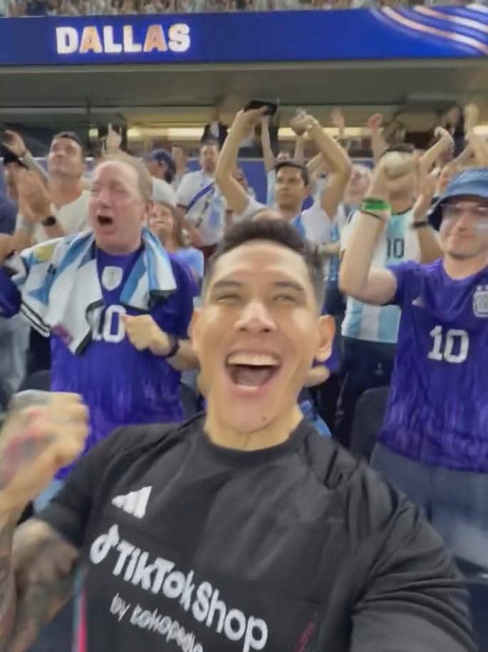 Seorang pria bersorak gembira di stadion bersama para pendukung Argentina yang mengenakan jersey biru putih di Dallas.