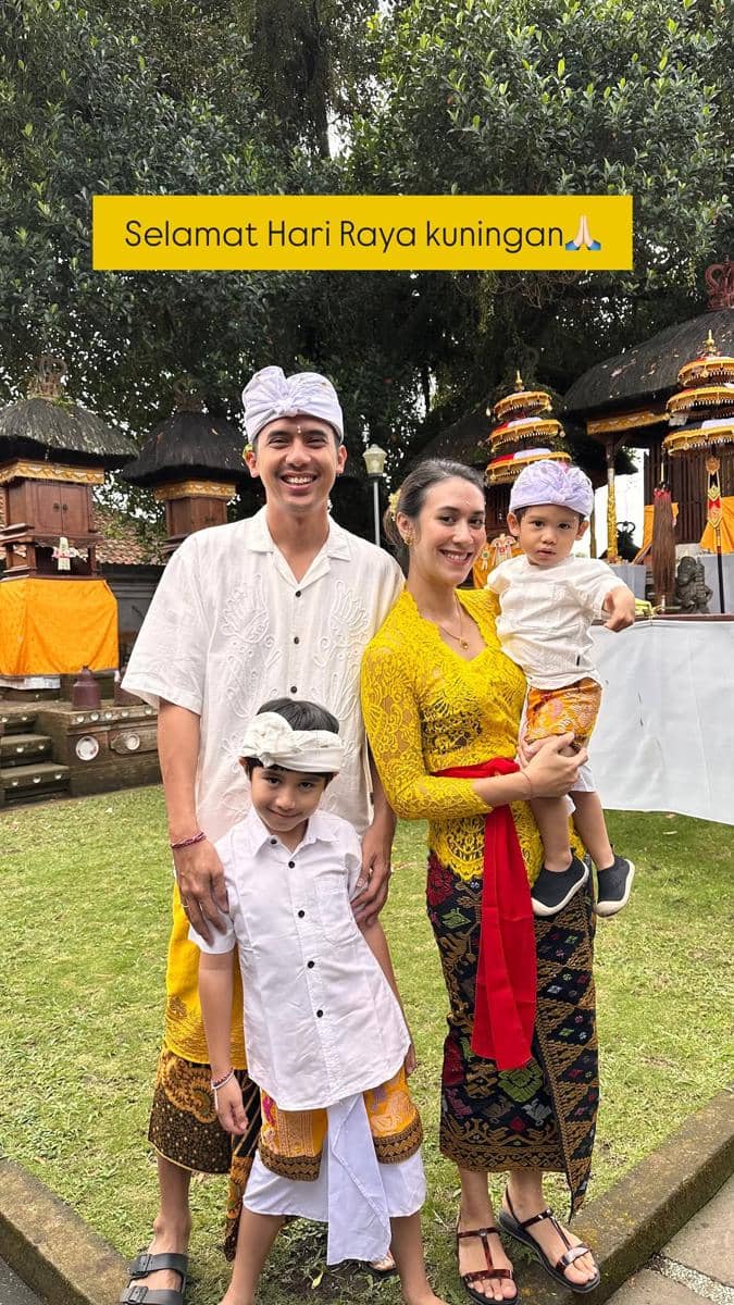 Sebuah keluarga mengenakan busana adat Bali berwarna putih dan kuning saat merayakan Hari Raya Kuningan di pura.